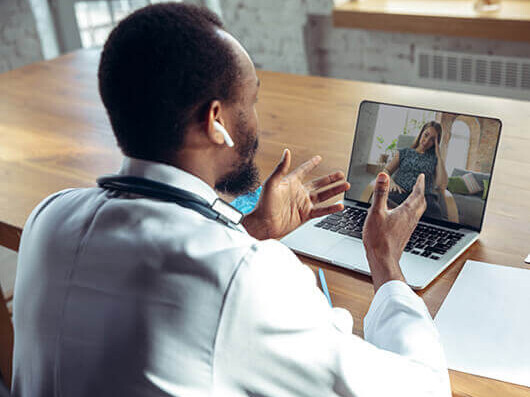 A doctor conducts a telemedicine appointment with a female patient using a laptop.