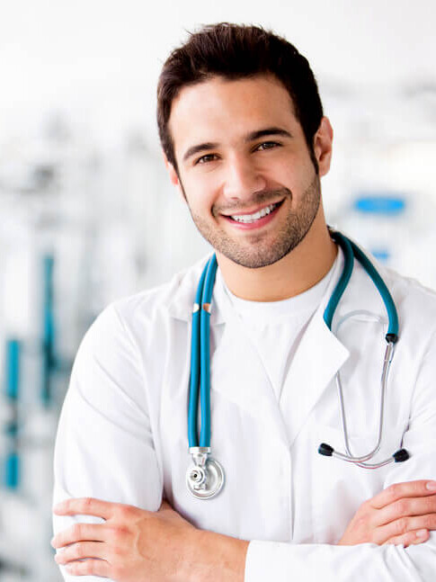 Male healthcare professional smiling in a clinical environment with stethoscope around neck.