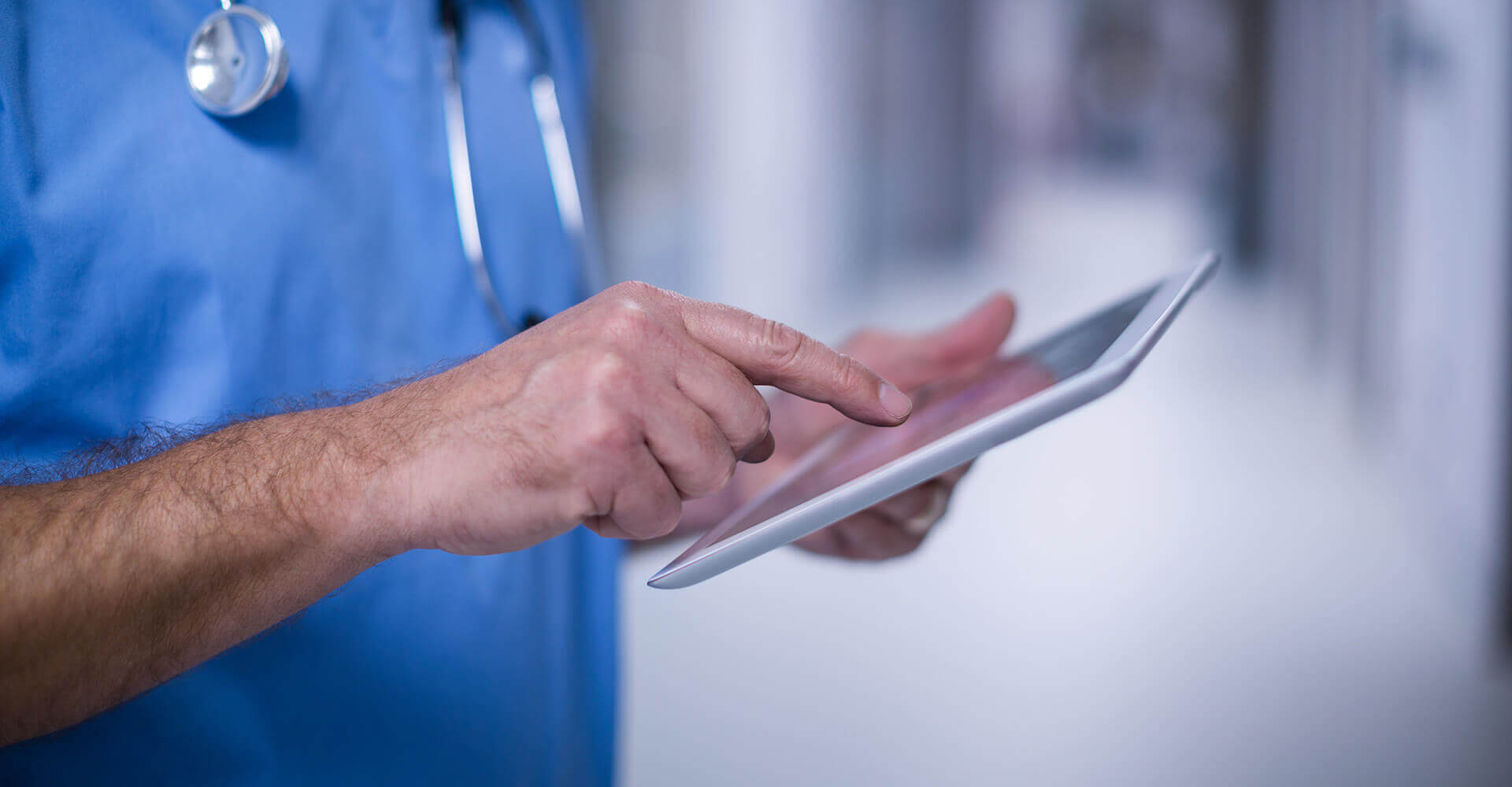 Healthcare professional in scrubs using a digital tablet.
